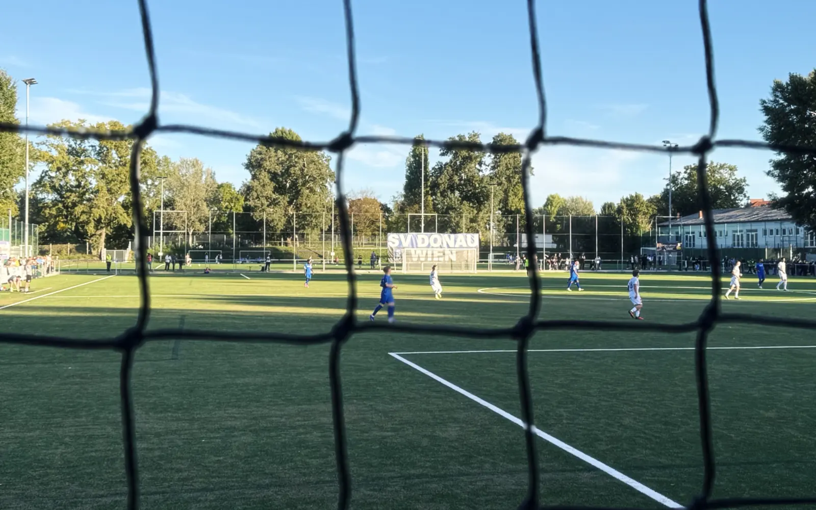 Blick durchs Tornetz auf ein Heimspiel am Weissauweg, im Hintergrund das Banner „SV Donau Wien“